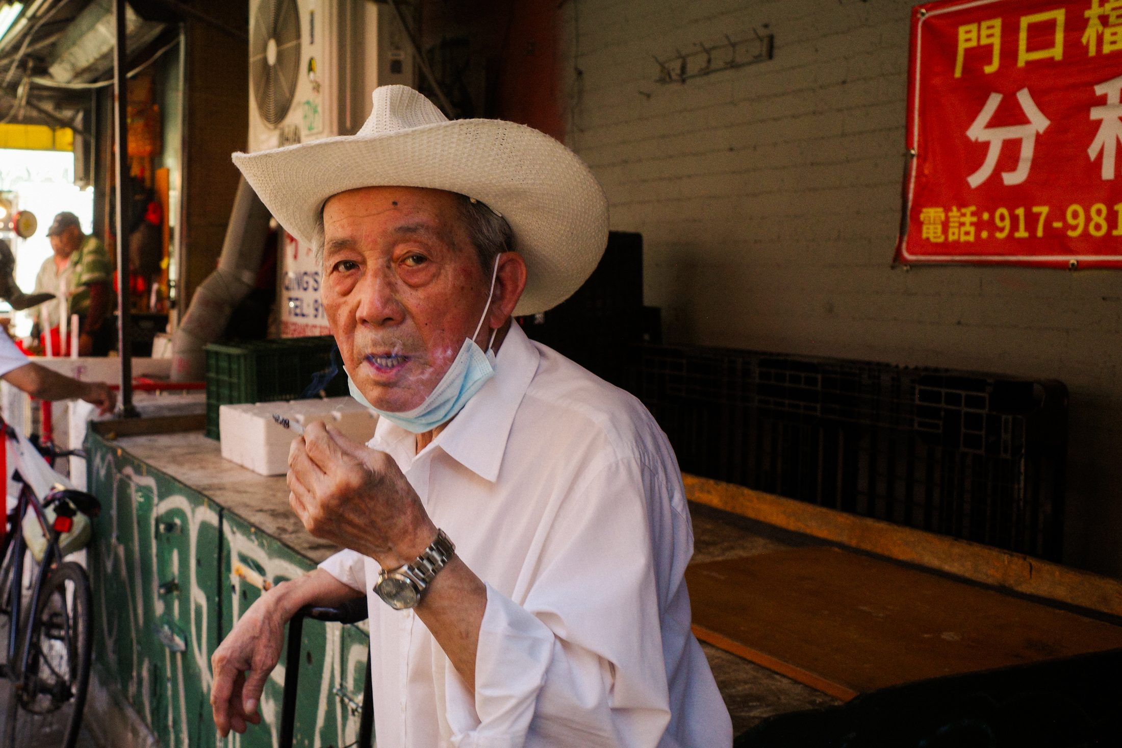 Elderly man in a white cowboy hat smoking, Chinatown storefront